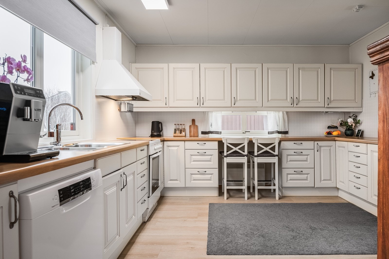 Stort kjøkken med profilerte fronter på over- og underskap, laminert benkeplate og fliser i benkerygg. Galleribilde