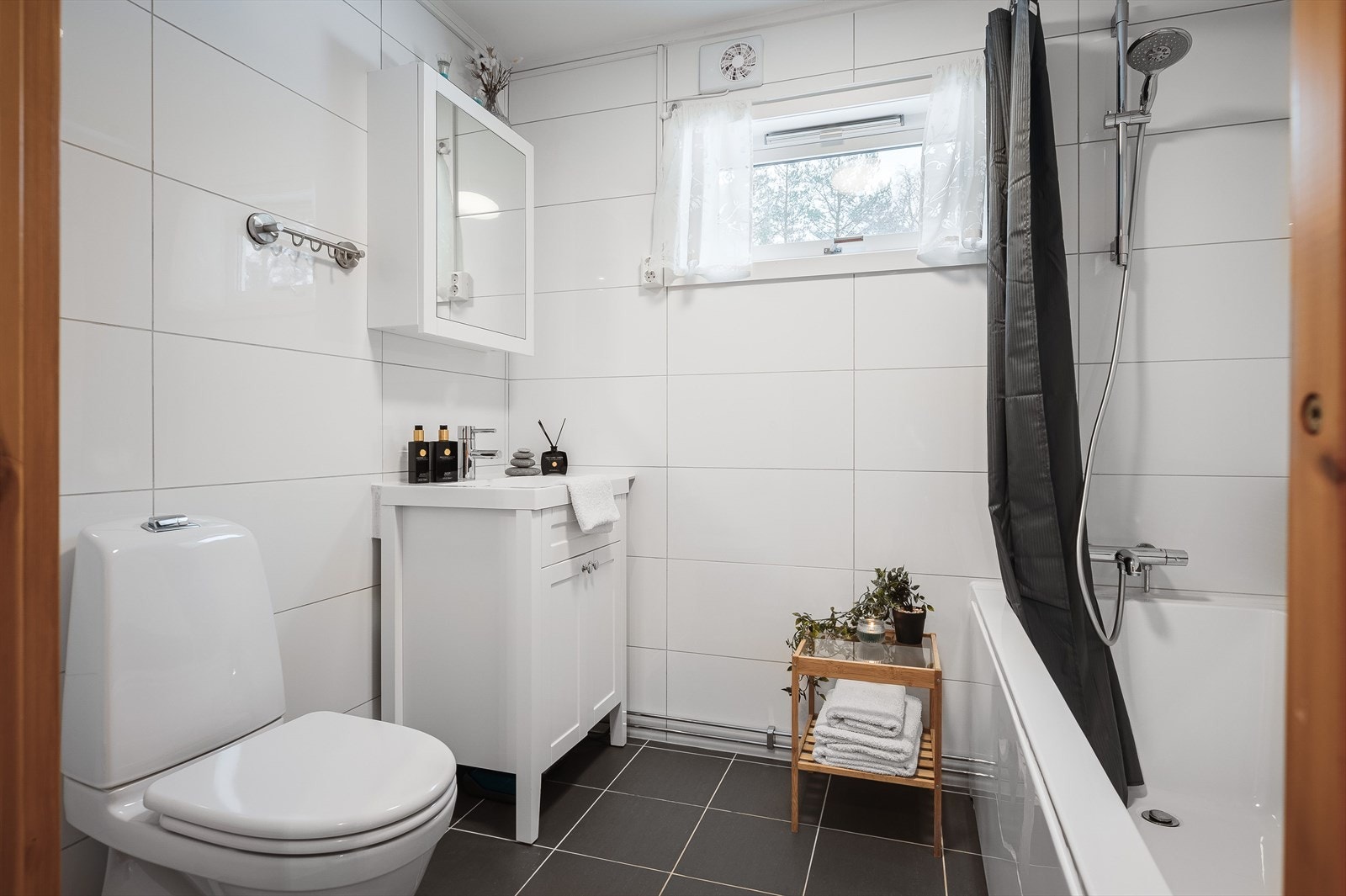 Bad i 1. etasje med flislagte gulv med gulvvarme og flislagte vegger. Badet har servant på underskap med speilskap over, gulvstående toalett og badekar med vegghengt dusj. Galleribilde