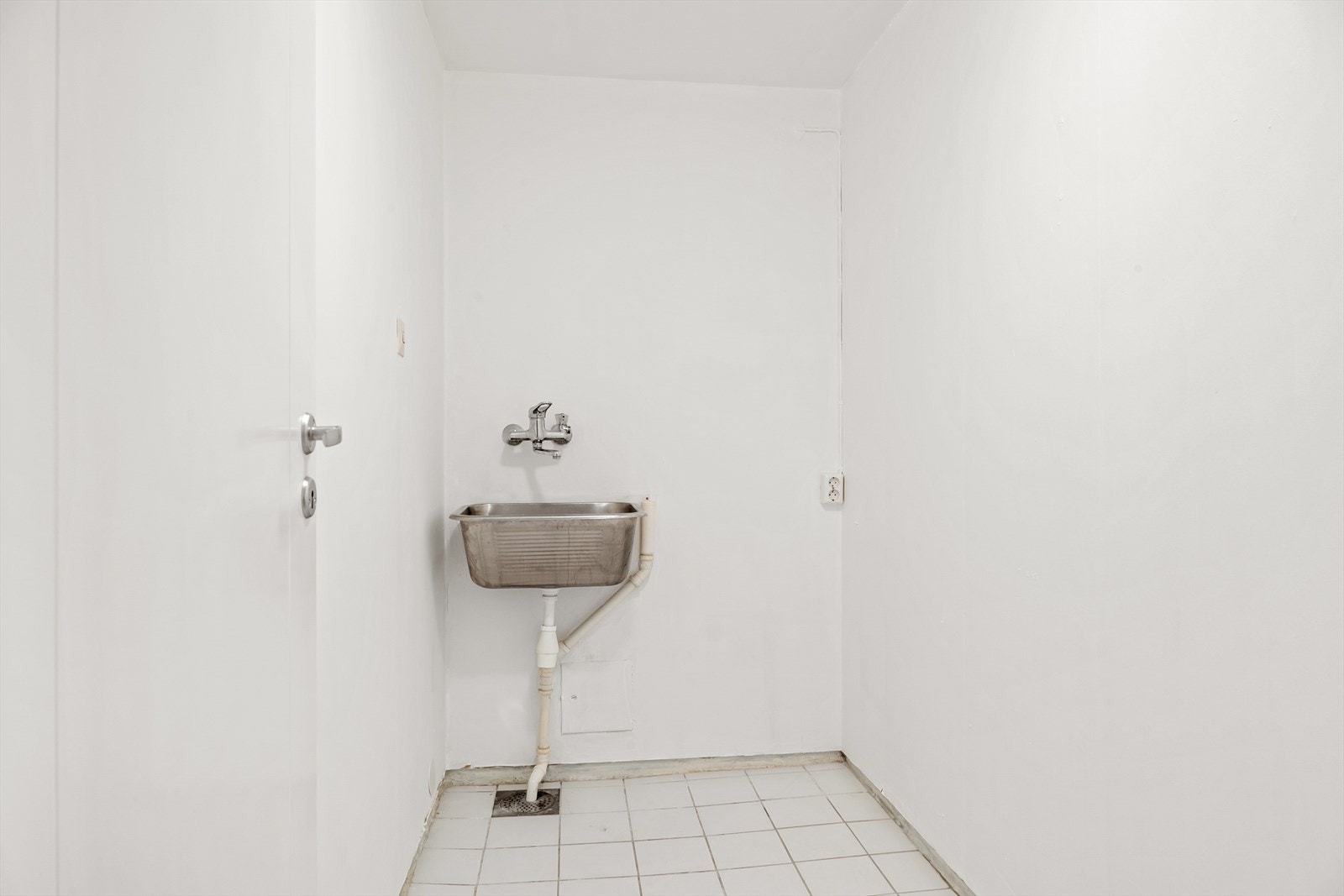 Vegg i vegg med badet er det eget vaskerom med fliser på gulv og utslagsvask. Galleribilde