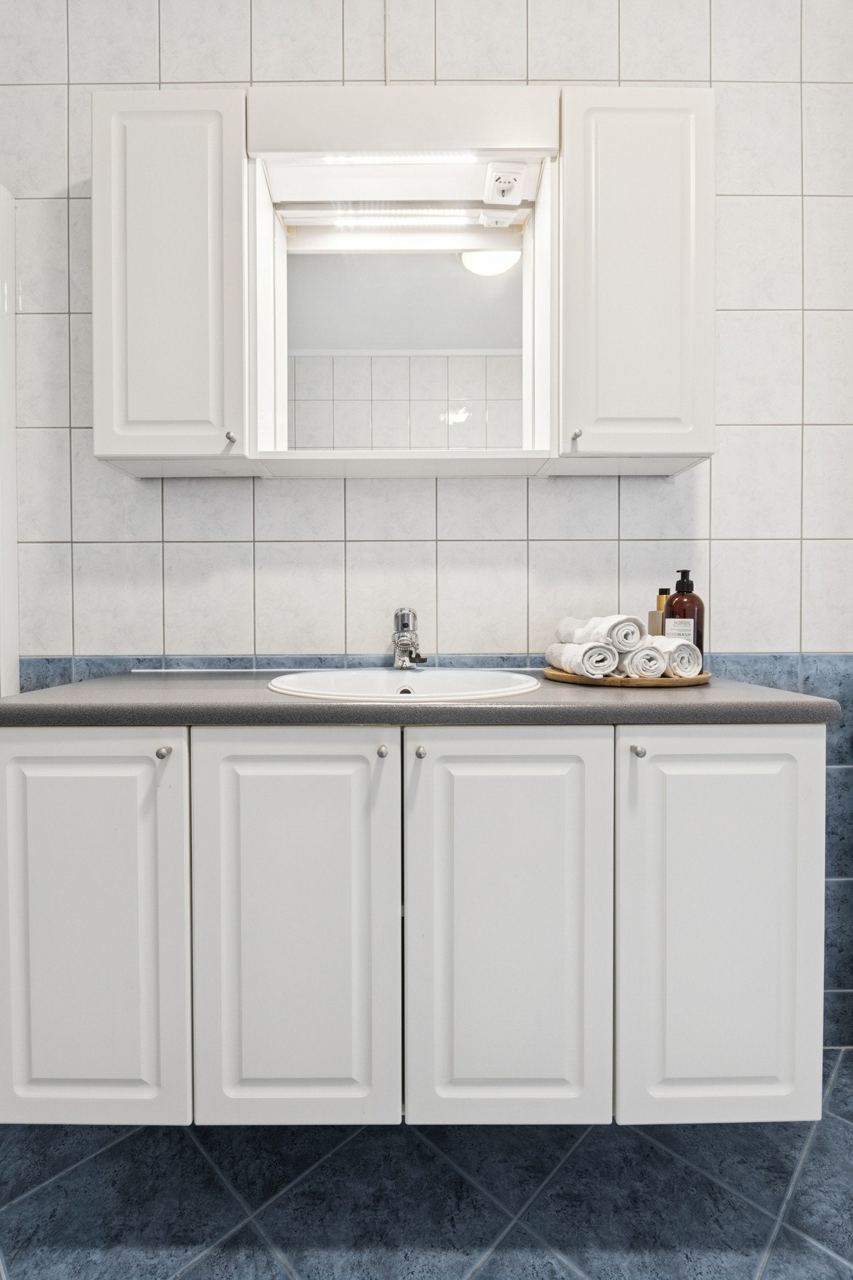 Rommet er innredet med servant, speil med lys, overskap og underskap, gulvstående toalett, dusjhjørne og opplegg for vaskemaskin. Galleribilde