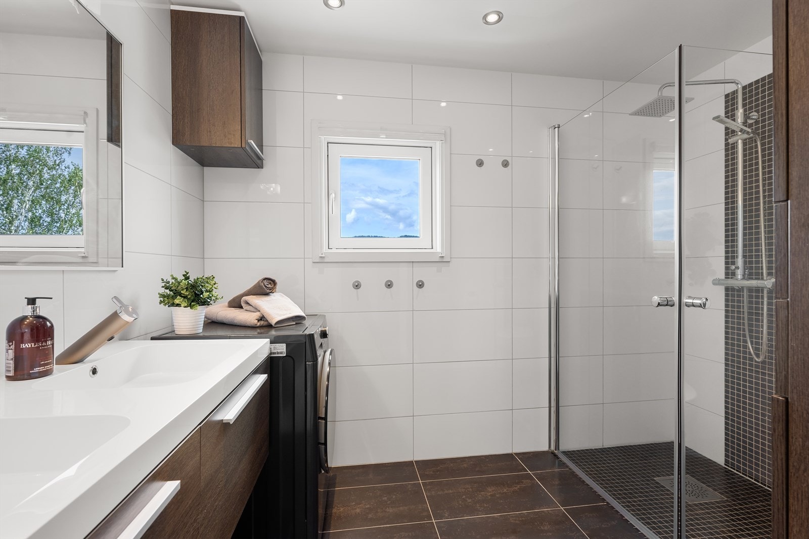 Innredning bestående av servant med underskap, speil med lys over, høyskap, overskap, dusjhjørne med svingbare glassdører, veggmontert toalett med innebygget sisterne og opplegg for vaskemaskin. Galleribilde