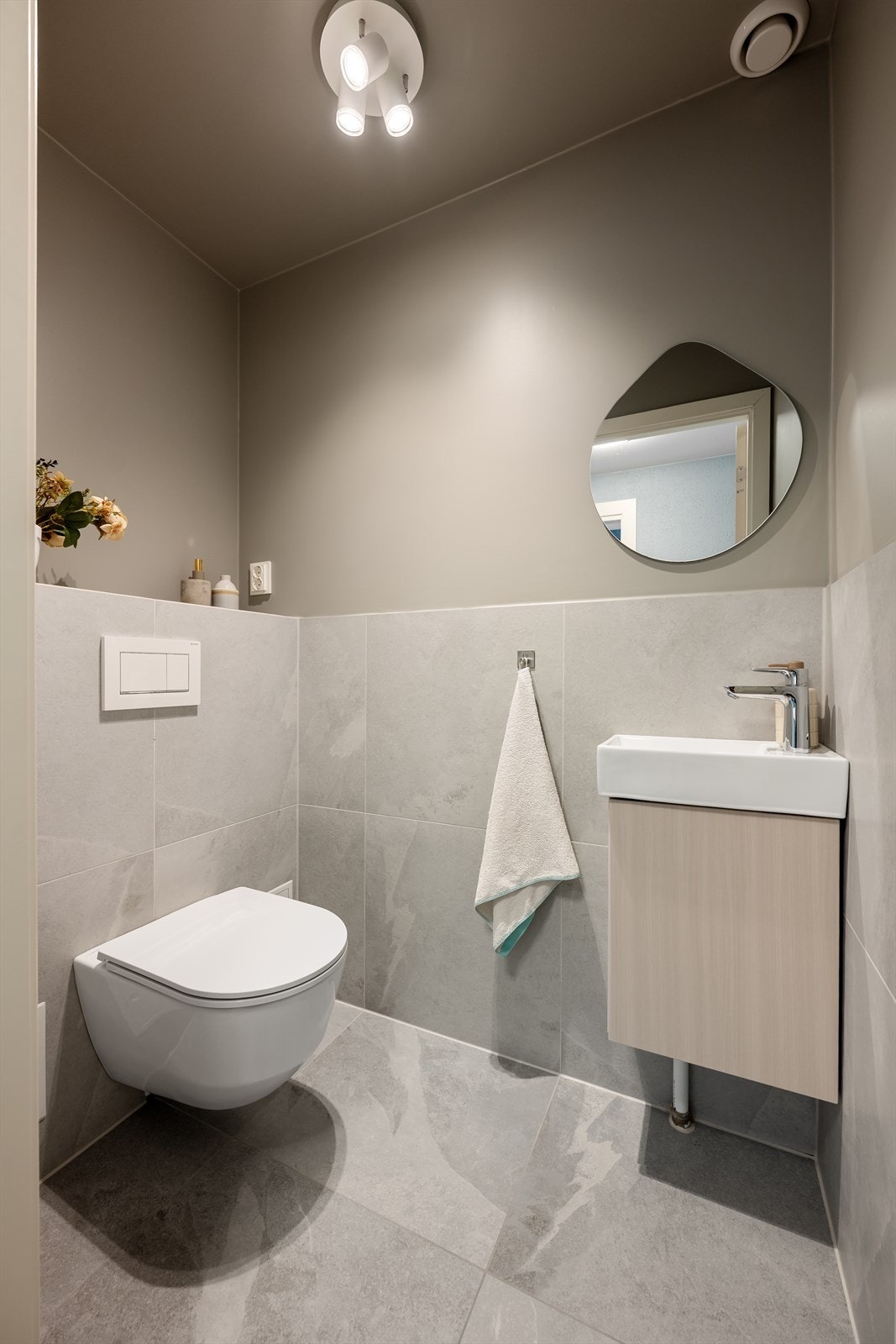 Flislagt toalettrom med elektrisk gulvvarme og innredning bestående av servant med underskap, speil og veggmontert toalett med innebygget sisterne. Galleribilde