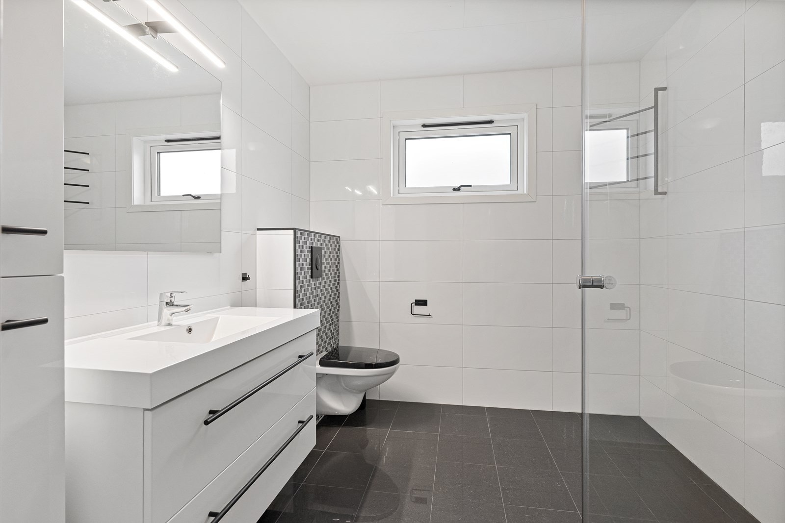 Lyst og moderne bad med stilrene fliser. Praktisk innredning og vindu for naturlig lys. Galleribilde