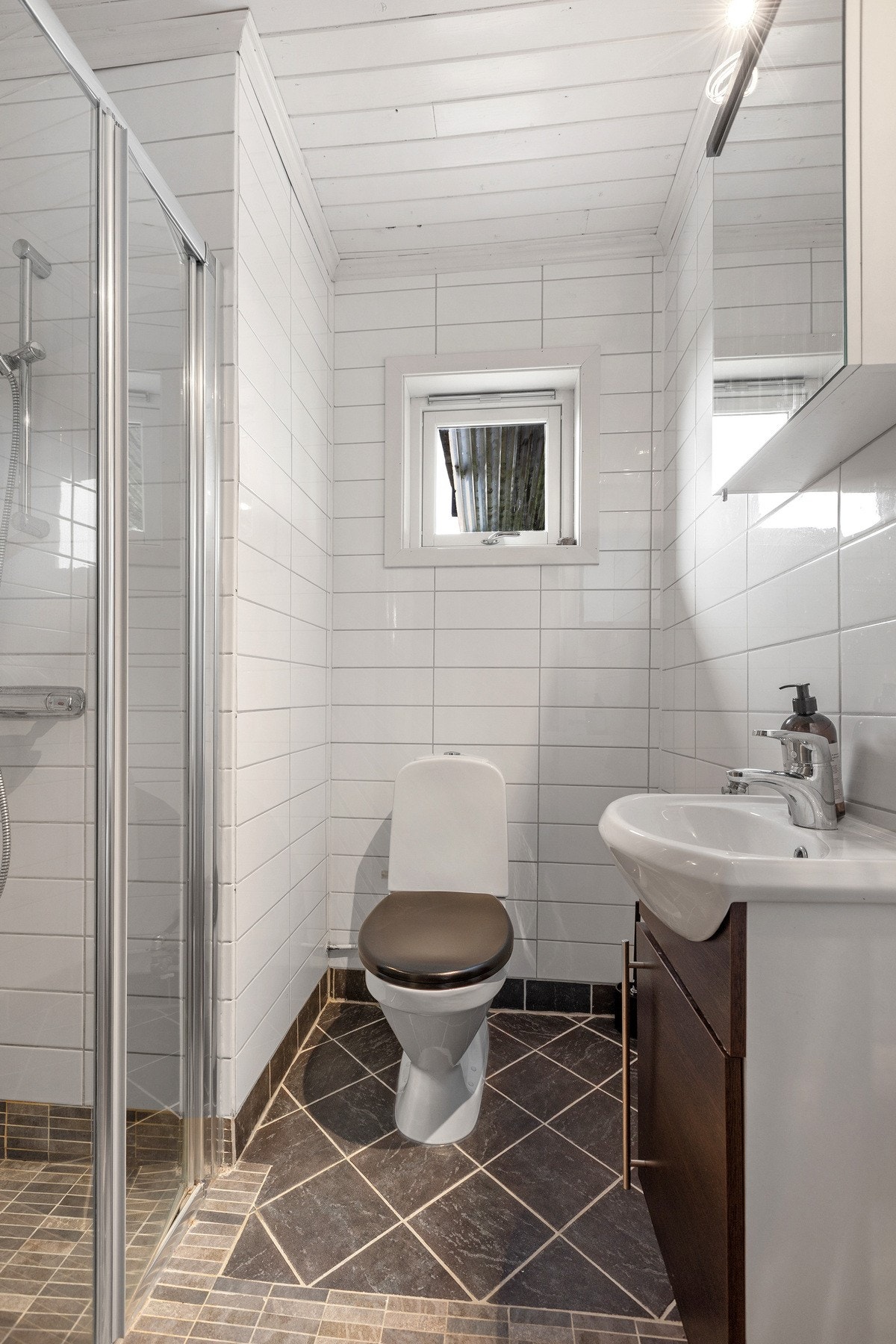 Badet i sokkel har dusjhjørne, toalett og innredning med speilskap over. Galleribilde