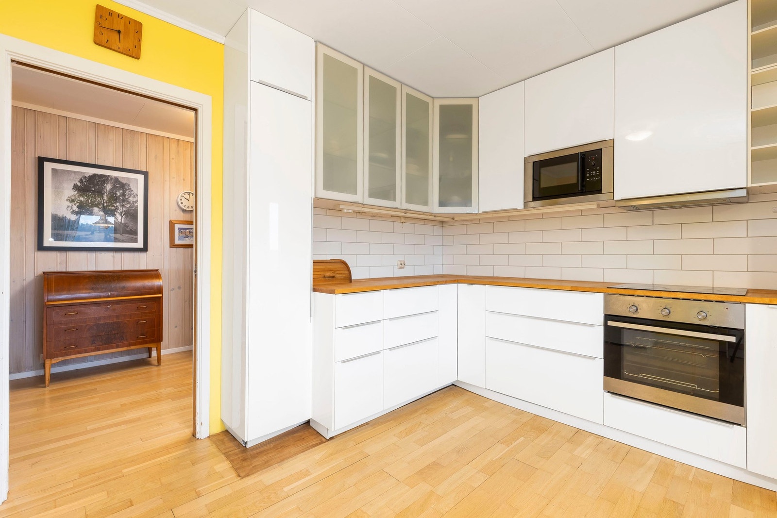 Kjøkkenet har en praktisk layout med folierte skrog og glatte fronter, noen med glassfelt for enkel oversikt. Galleribilde