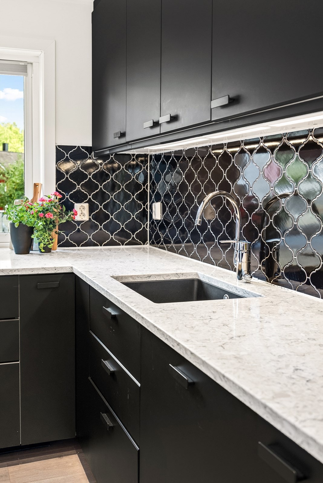 Det er montert fliser på vegg over benkeplate og kjøkkenventilator over kokesone med avtrekk ut. Galleribilde