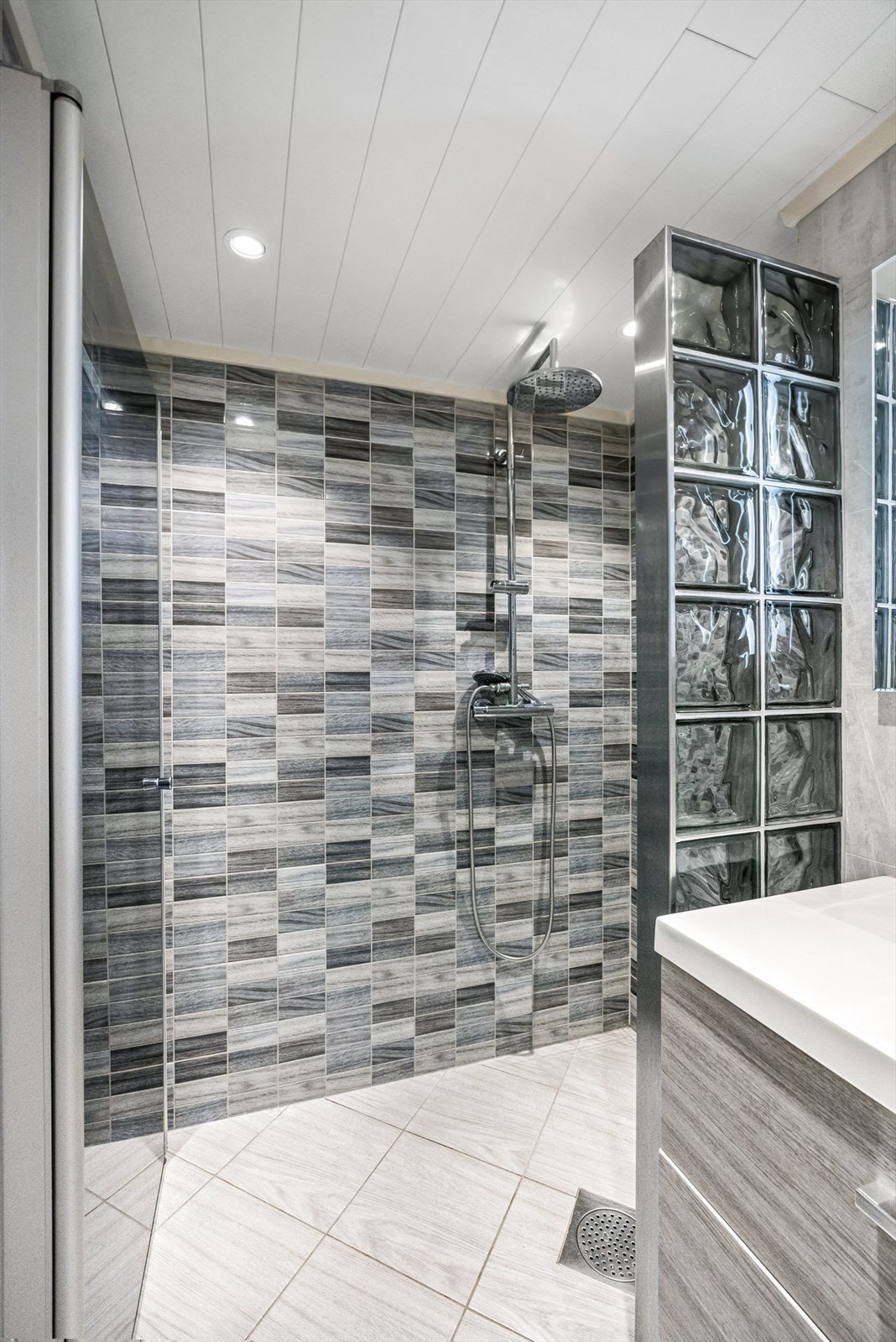 Badet er innredet med servantskap med ett-greps blandebatteri, speil med lys, høyskap, vegghengt toalett med innebygget sisterne, avskjermet dusjhjørne med glassbyggerstein, blandebatteri og dusjgarnityr. Galleribilde