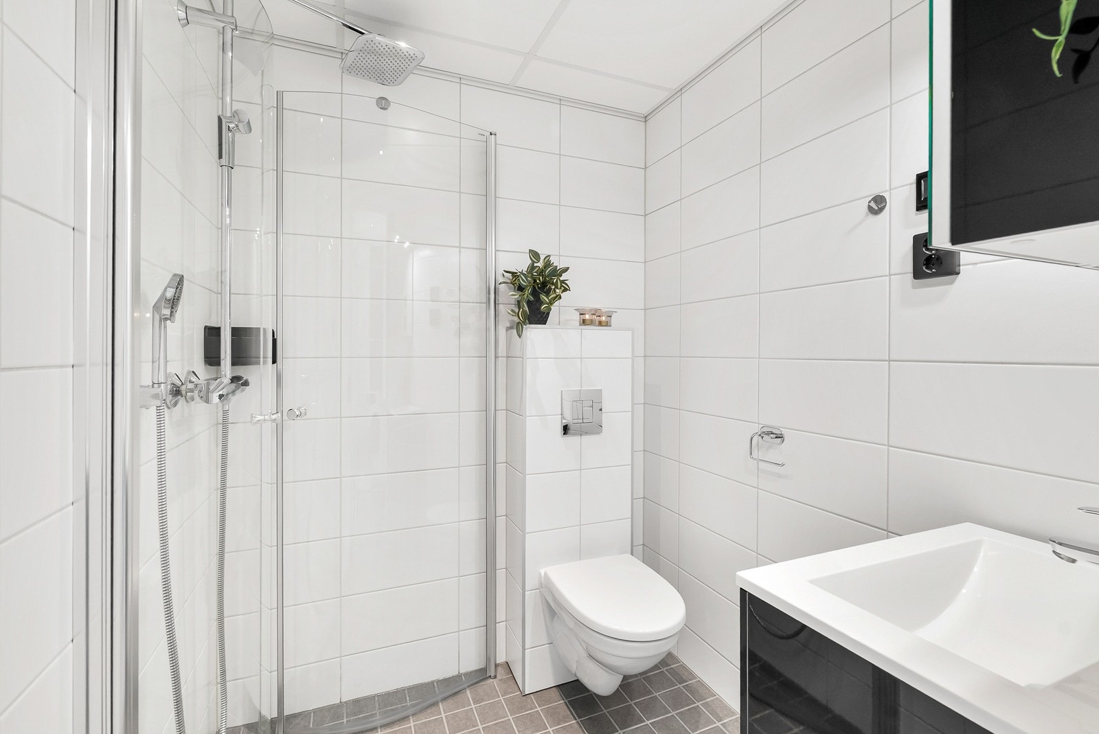 Pent og tidløst flislagt bad med varmekabler i gulv. Downlights i himling. Dusjhjørne med innfellbare vegger. Vegghengt toalett. Galleribilde