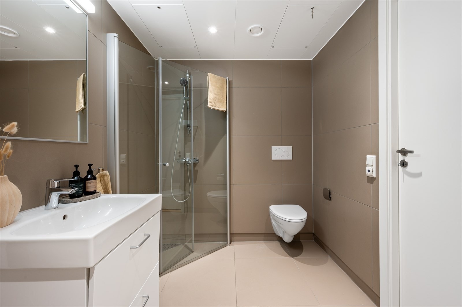 - Badet er utstyrt med dusjdører i glass, vegghengt toalett, servant med underskap og opplegg for vaskemaskin - Galleribilde