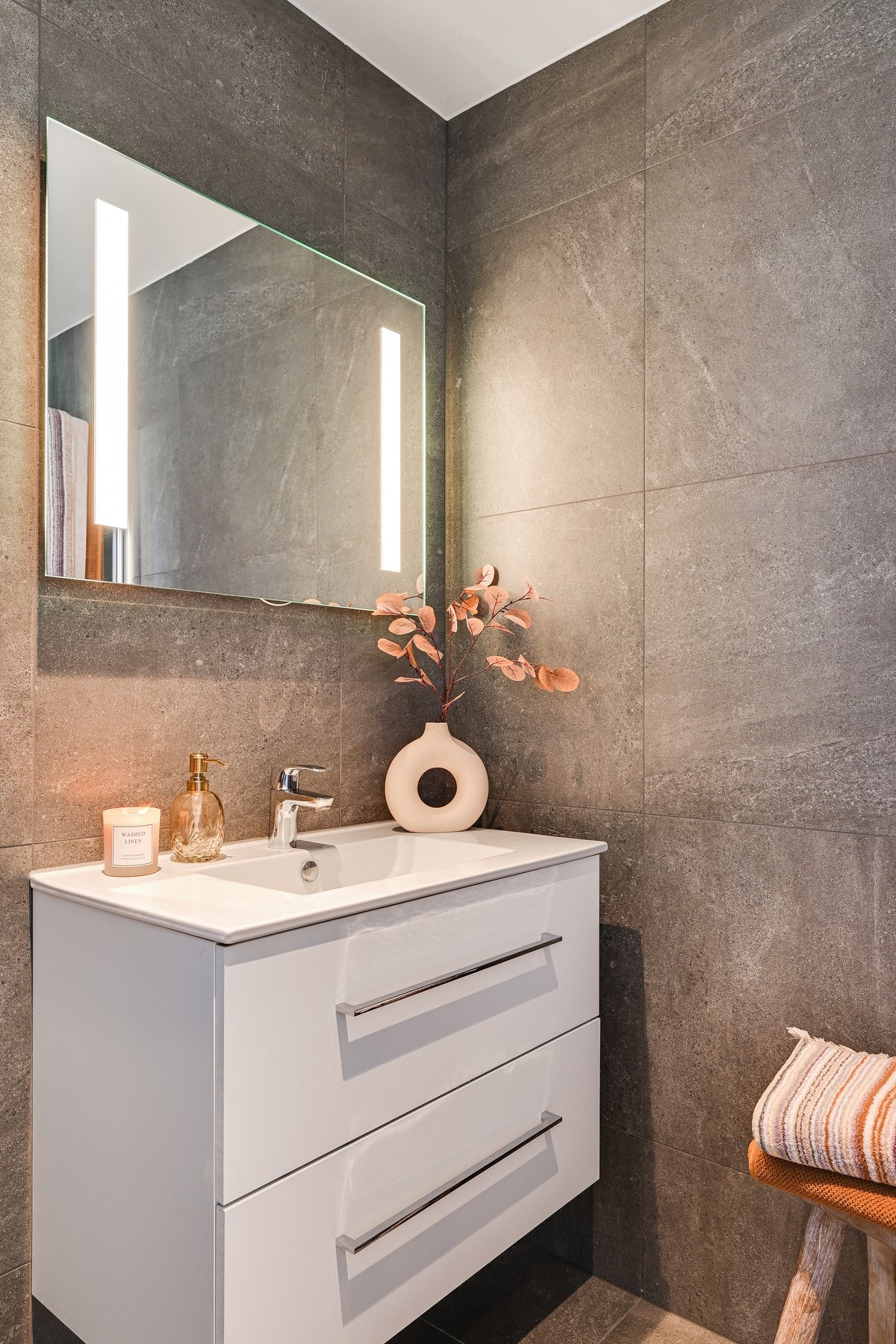 Badet inneholder servant med skuffer, speil med lys, veggmontert wc og dusjhjørne. Galleribilde