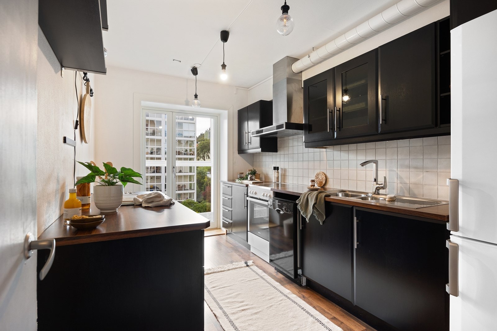 Kjøkken med sorte glatte fronter, laminat benkeplate, to dører med glassfelt, integrert oppvaskmaskin, kjøl- og fryseskap. Galleribilde