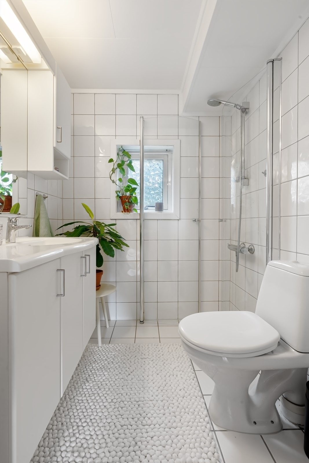 Flislagt bad med varmekabler i gulv. Hjørnedusj med glassdører, toalett, servant med skap og speil med belysning og skap. Galleribilde