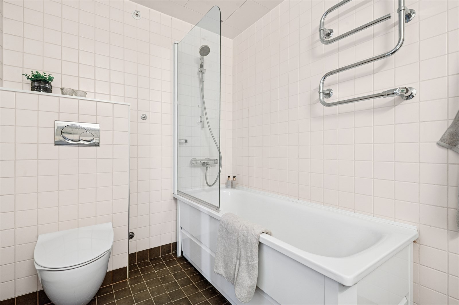 På badet er det hel servantplate med servantskap, veggfestet toalett med skjult sisterne, badekar med glass dusjvegg og opplegg for vaskemaskin. Galleribilde
