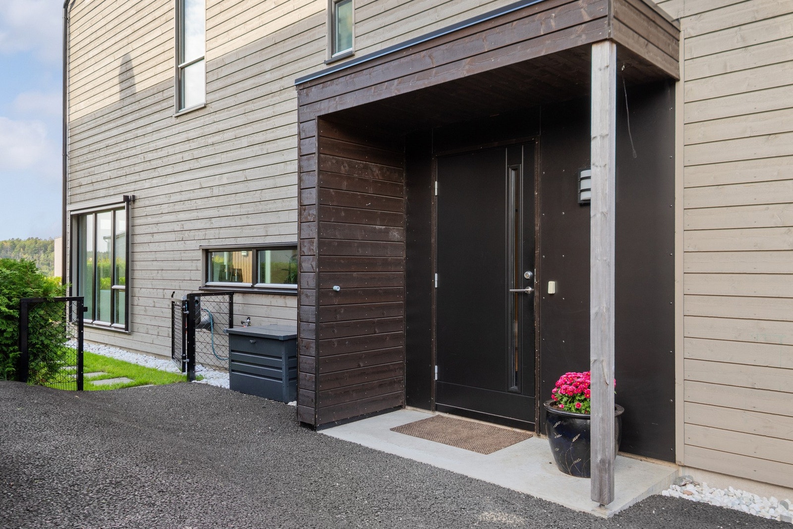 Boligen har et overbygd inngangsparti med støpt velkomsttram, belysning og sort dør. Galleribilde