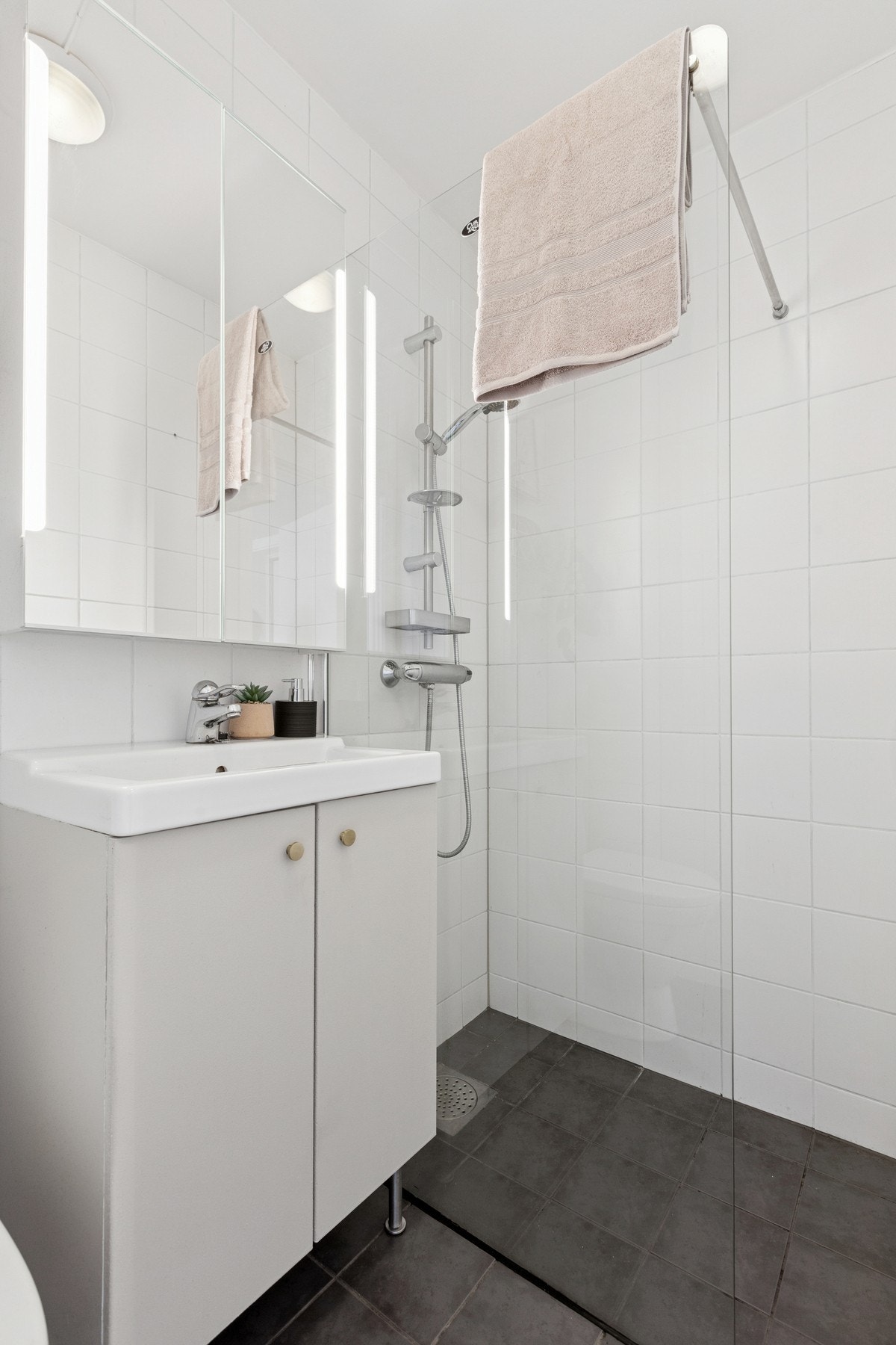 Lyst og flislagt baderom utstyrt med dusjnisje, servantskap, speilskap med lys og toalett. Galleribilde