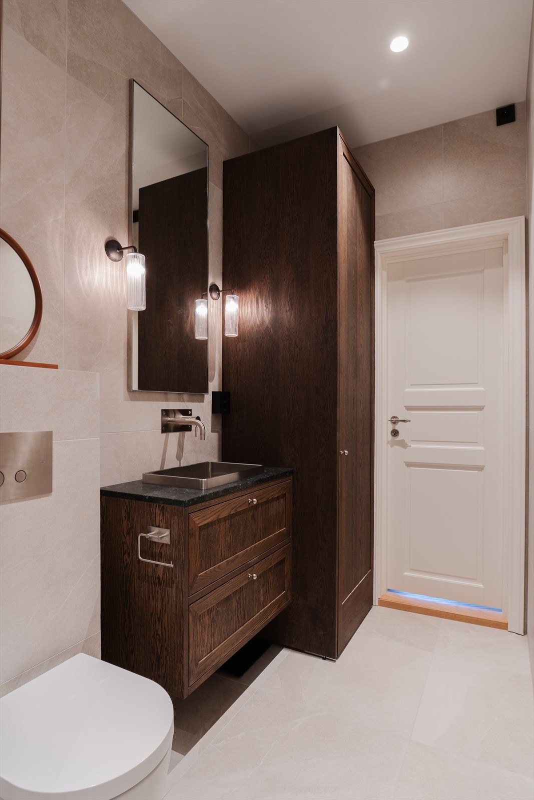 Baderomsinnredning bestående av benkeskap og høyskap med profilerte fronter. Benkeplate i komposittstein. Speil og belysning over servant Galleribilde