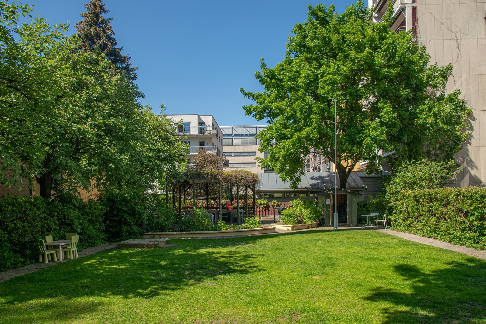 Gårdsrommet er frodig opparbeidet med grønn plen, diverse beplantning og pergola med sitteplasser og grill for beboerne. Galleribilde