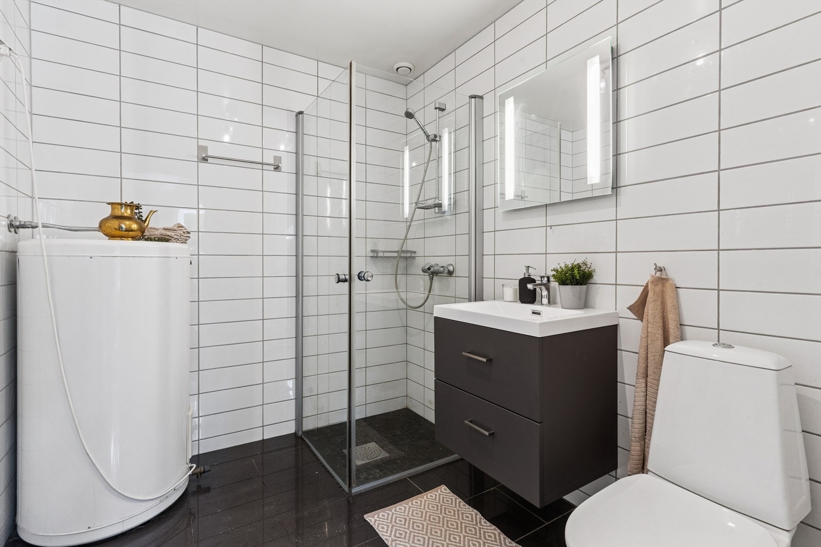 Badet i 1. etasje er flislagt med deilig gulvvarme, utstyrt med toalett, dusj, servant med ett-greps kran og skuffer og varmtvannsbereder. Galleribilde