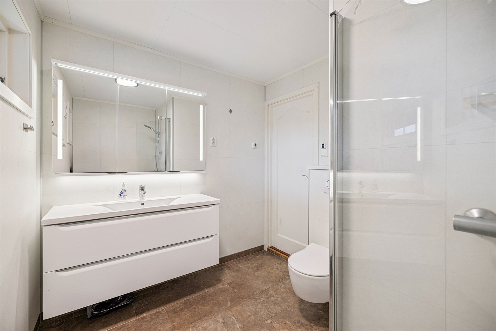 Badet er utstyrt med vegghengt toalett og dusjhjørne med glassdører Galleribilde