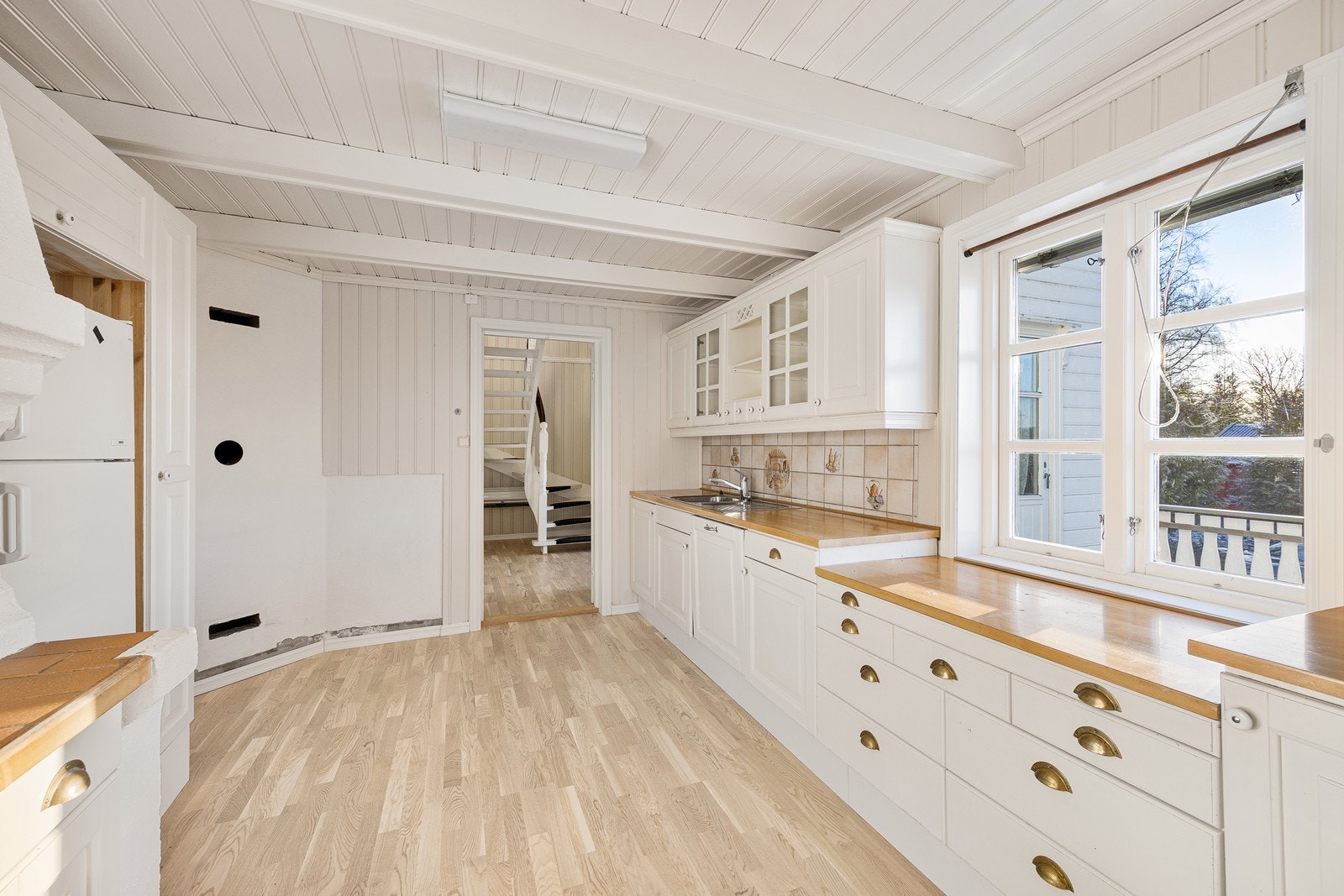 Kjøkkenet har en landlig innredning med lyse, profilerte fronter, vitrineskap, benkeplater i heltre og en nedfelt oppvaskkum. Galleribilde