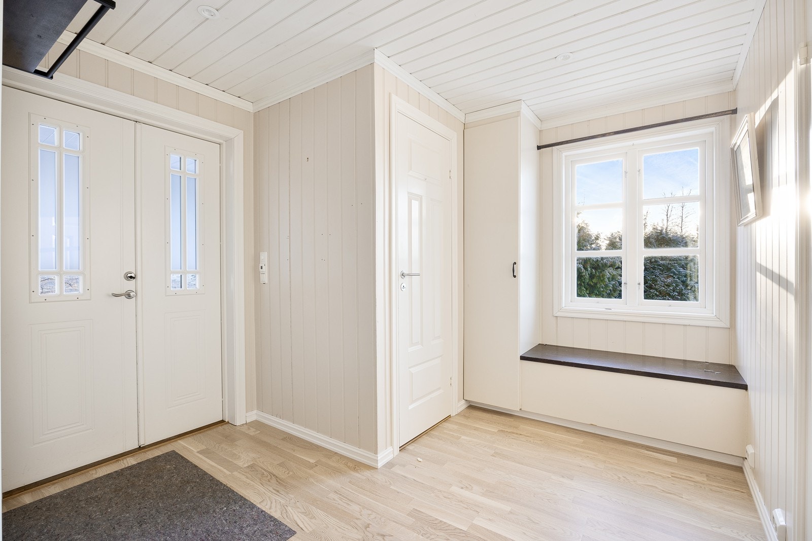 Den romslige entreen har lysmalte vegger og downlights. Det er plass til åpen garderobeløsning. Under vinduet er det sittebenk og et skap i forlengelsen av denne. Galleribilde