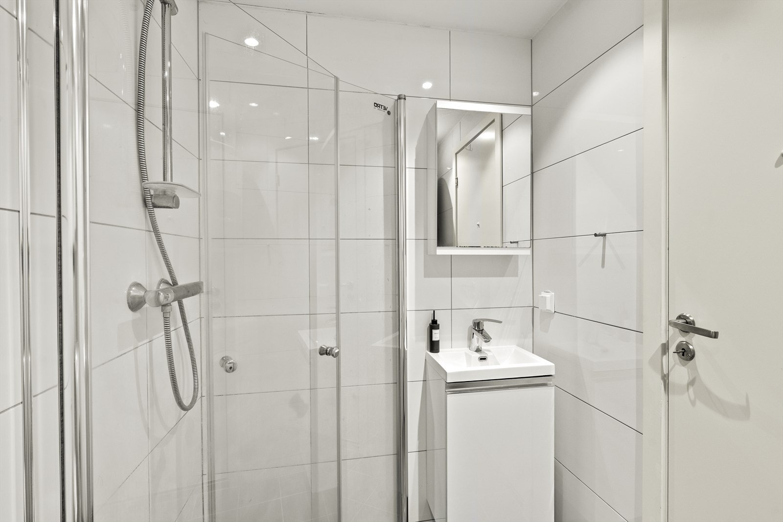 Her er det flislagte vegger og gulv med elektriske varmekabler samt downlights i himling. Badet er praktisk innredet med nedfelt servant, veggmontert toalett og dusjhjørne med foldedører i glass - som gir effektiv utnyttelse av plassen. Galleribilde
