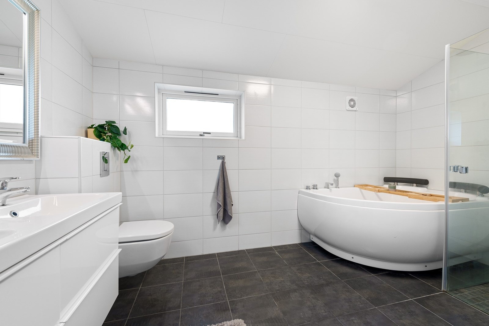 Stort baderom med badekar, dusjhjørne, toalett, servantinnredning og opplegg for vaskemaskin Galleribilde