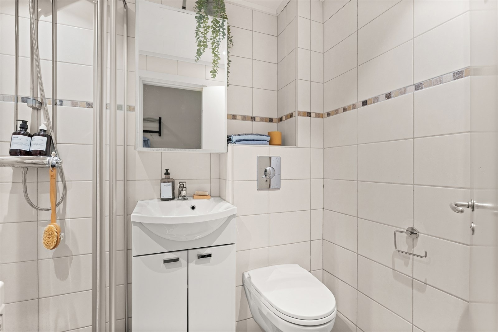 Badet har opplegg for vaskemaskin, servant med innredning, dusjhjørne med innfellbare dusjdører, toalett og varmekabler i gulv. Galleribilde