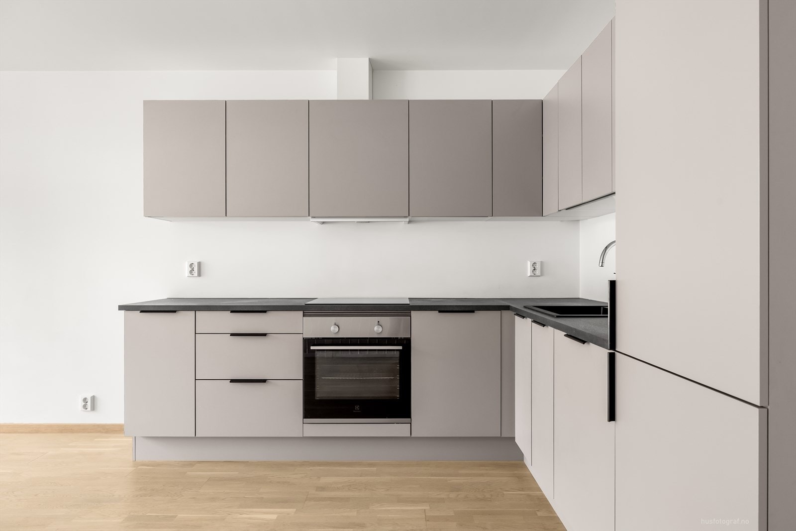 Delikat og stilrent kjøkkeninnredning i hjørne med mye skap og benkeplass. Kjøkkeninnredningen har moderne glatte fronter og benkeplate av laminat. Galleribilde