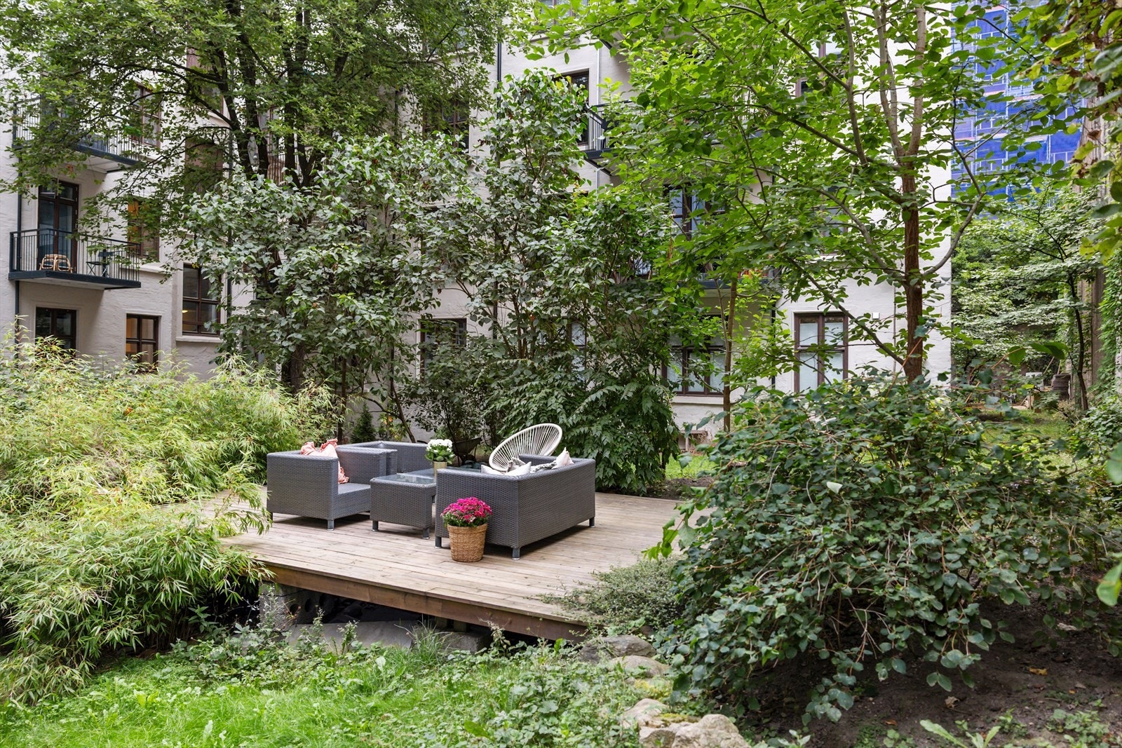 I bakgården ligger en liten terrasse med utemøbler, omgitt av frodige trær og beplantning. Galleribilde