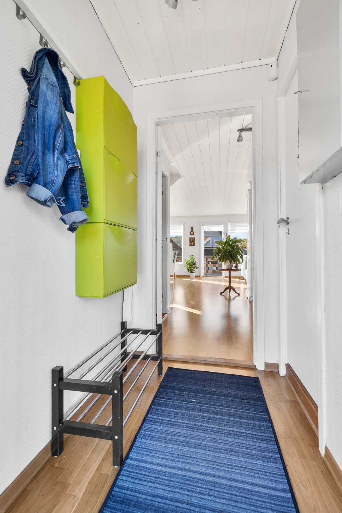 Lys gang med parkettgulv og hvite vegger, som leder inn til stuen. Galleribilde