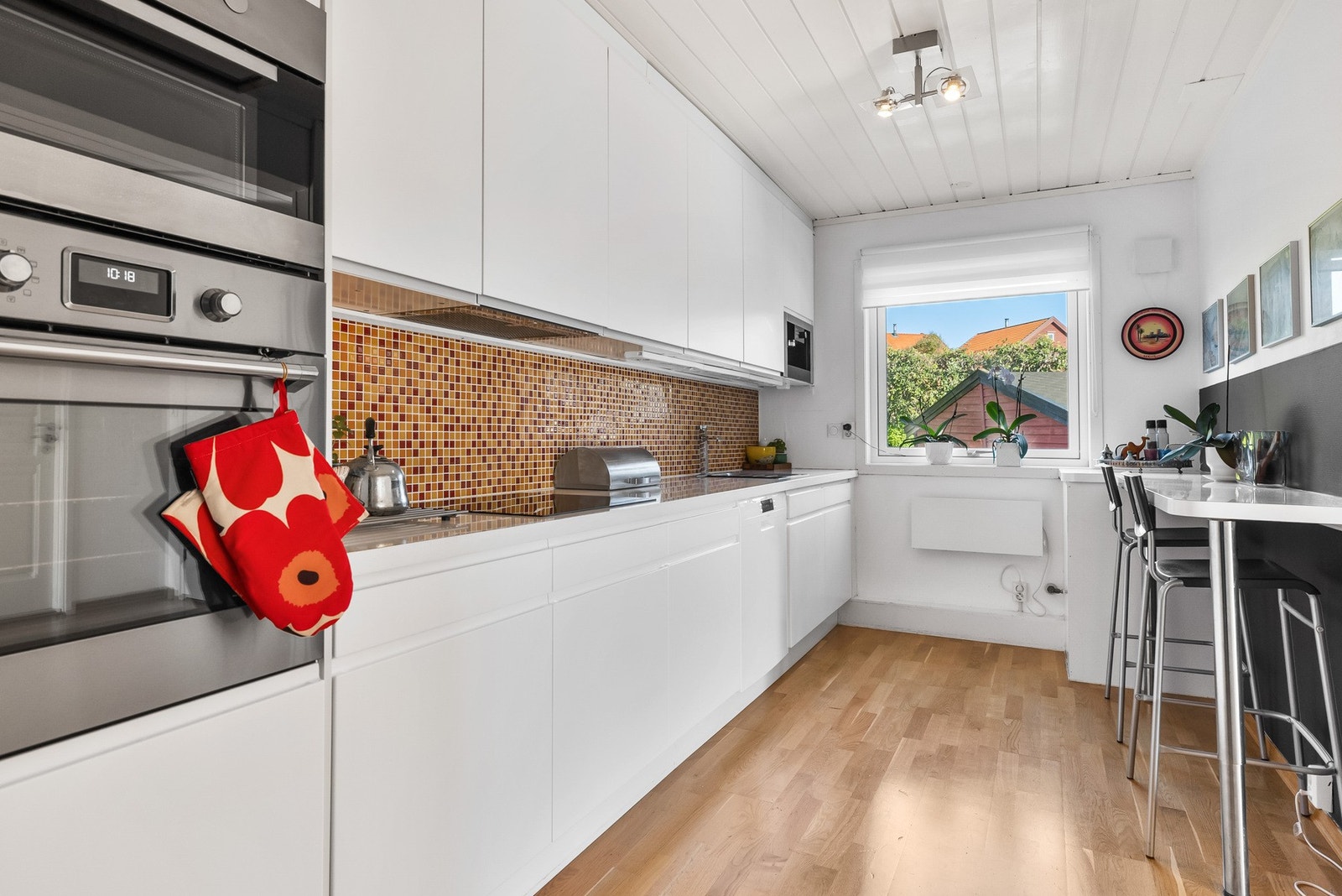 Moderne kjøkken med hvite skap, integrerte hvitevarer, mørk vegg og flislagt bakvegg. Lys parkettgulv. Galleribilde