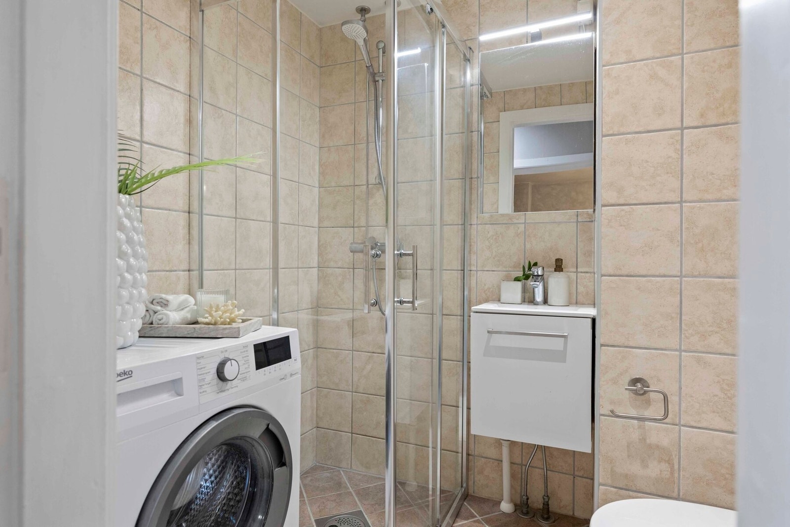 Badet har dusjhjørne med innfellbare dusjvegger og baderomsinnredning med servant. Overskap med speil og lys. Galleribilde