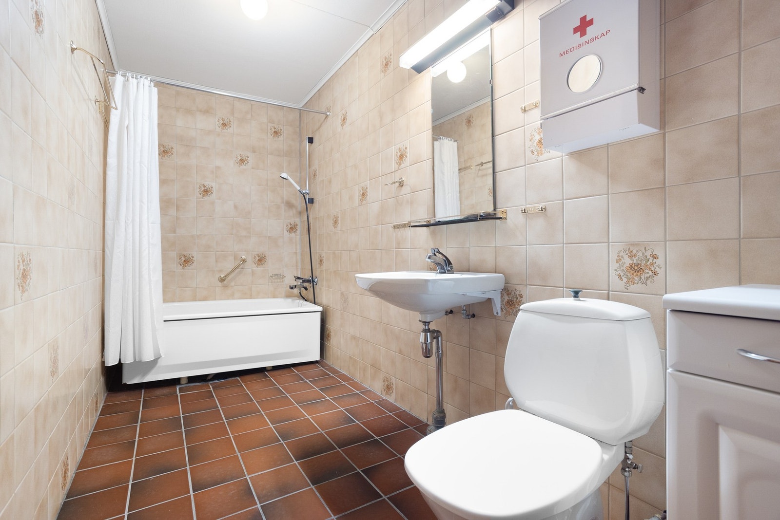 Baderom med flislagte overflater. Baderommet inneholder badekar med dusjmulighet, toalett og servant. Galleribilde