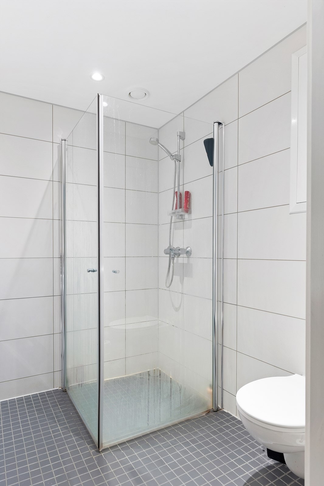 Videre er badet innredet med servantskap med speil og lys, dusjhjørne og vegghengt toalett. Galleribilde