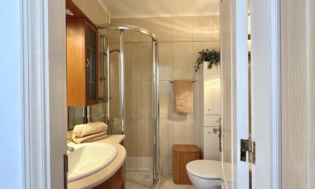 Badet har flislagte gulv og vegger, dusjkabinett, pent baderomsmøbel og frontmatet vaskemaskin Galleribilde