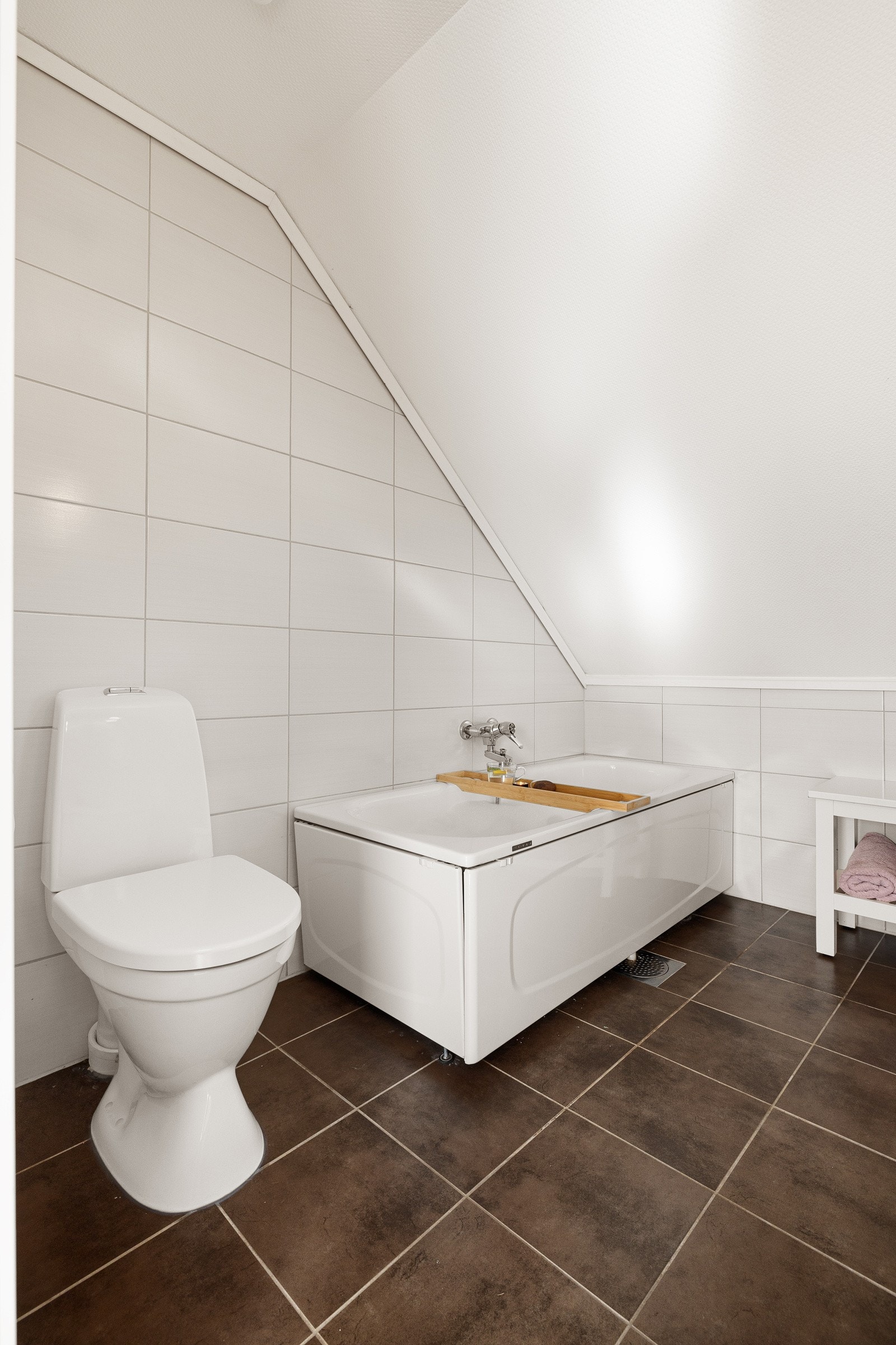 Praktisk badekar med veggmontert ett-greps armatur, gulvstående toalett, vegghengt servantinnredning med slette skuffefronter, samt heldekkende servant med ett-greps armatur. Galleribilde