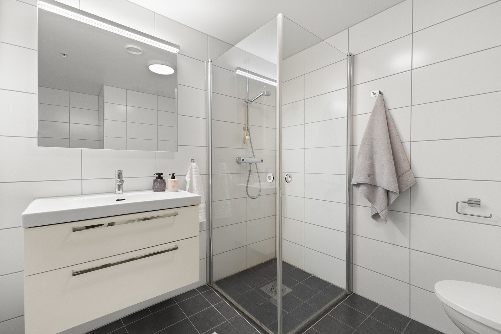 Badet er utstyrt med dusjhjørne, vegghengt toalett, servant, og opplegg for vaskemaskin. Galleribilde