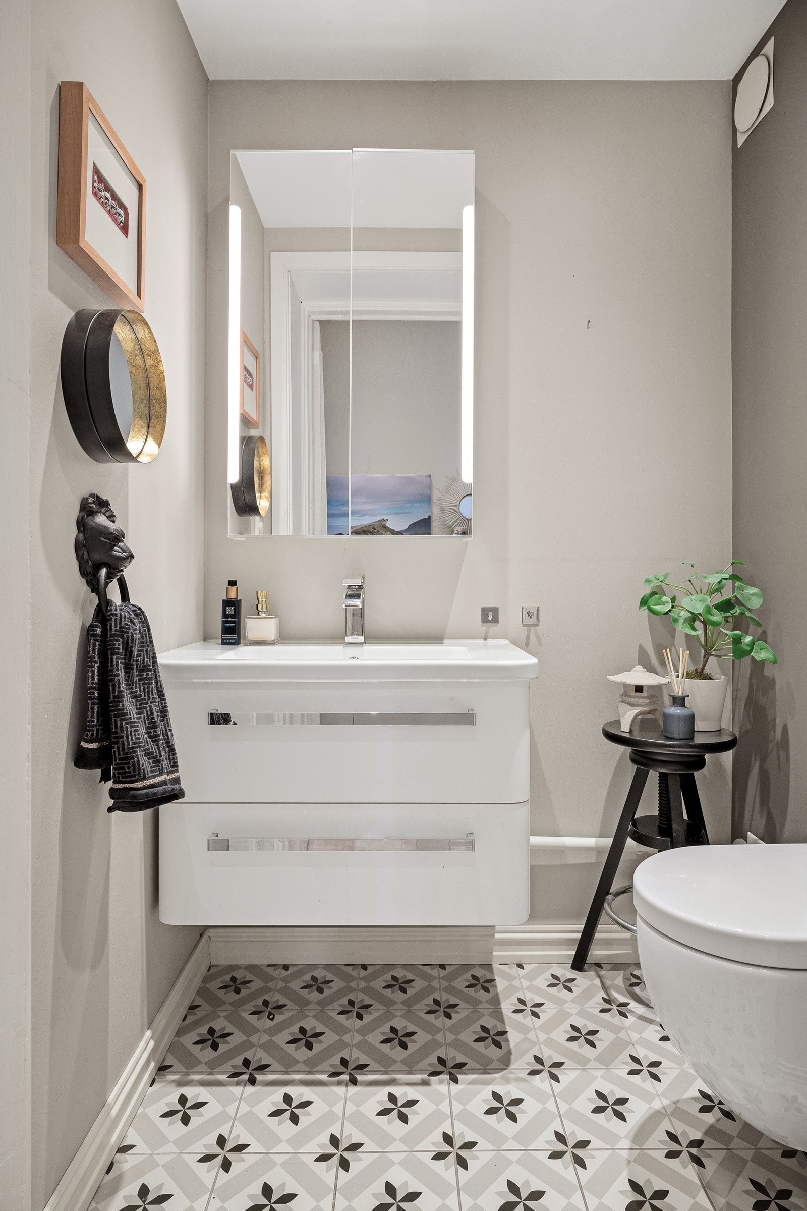 Flott wc med fine fliser på gulv, vegghengt toalett og servantinnredning med skuffer, og speilskap over Galleribilde