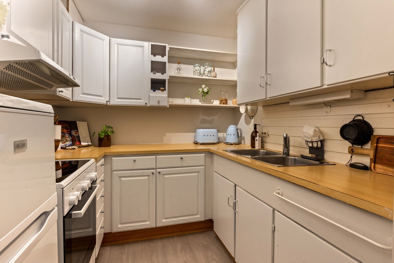 Den hvite kjøkkeninnredningen er klassisk og tidløs, utstyrt med profilerte fronter, laminert benkeplate, frittstående komfyr og kjøl/fryseskap, og her medfølger alle hvitevarer salget Galleribilde