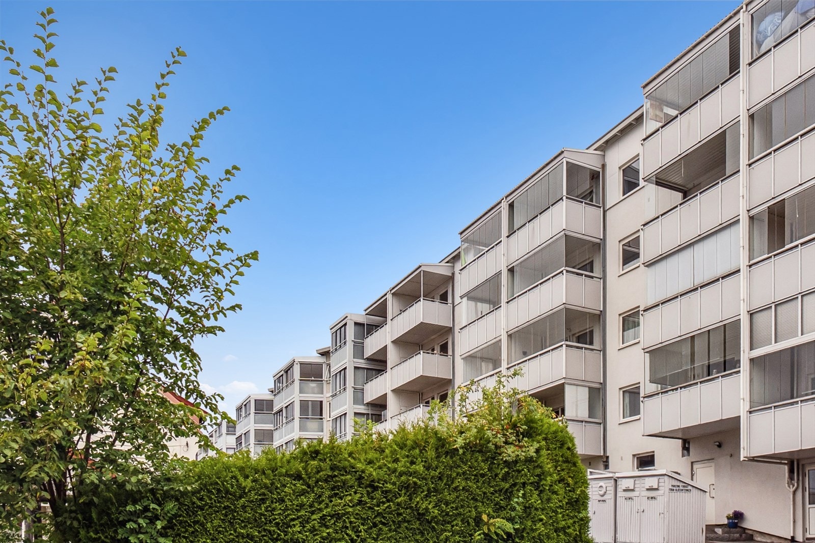 Pent opparbeidet felleshage foran bygget med plen, sittegrupper og beplantning. Galleribilde