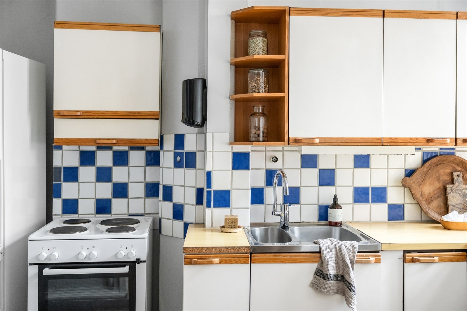 Eldre kjøkkeninnredning med slette fronter, fliser og enkel belysning over laminat benkeplate med nedfelt oppvaskkum m/ bl.batteri. Galleribilde