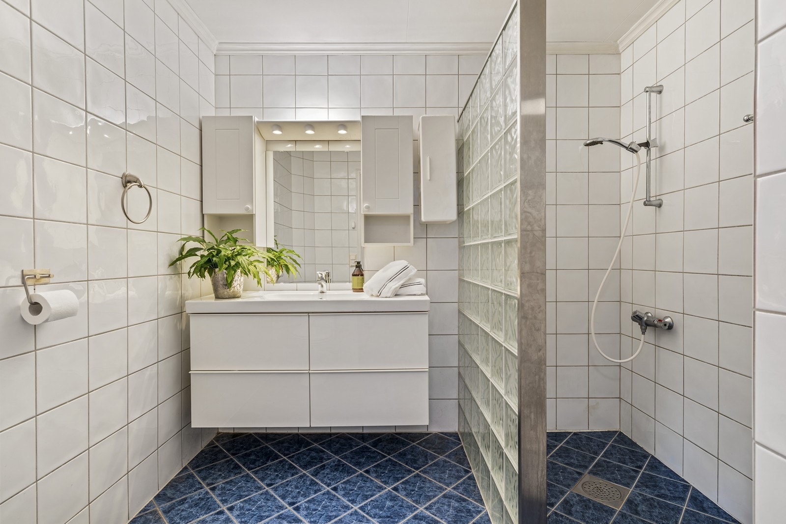 Pent, flislagt baderom med skuffeseksjon i høyglans og dusjhjørne med glassbyggerstein. Galleribilde