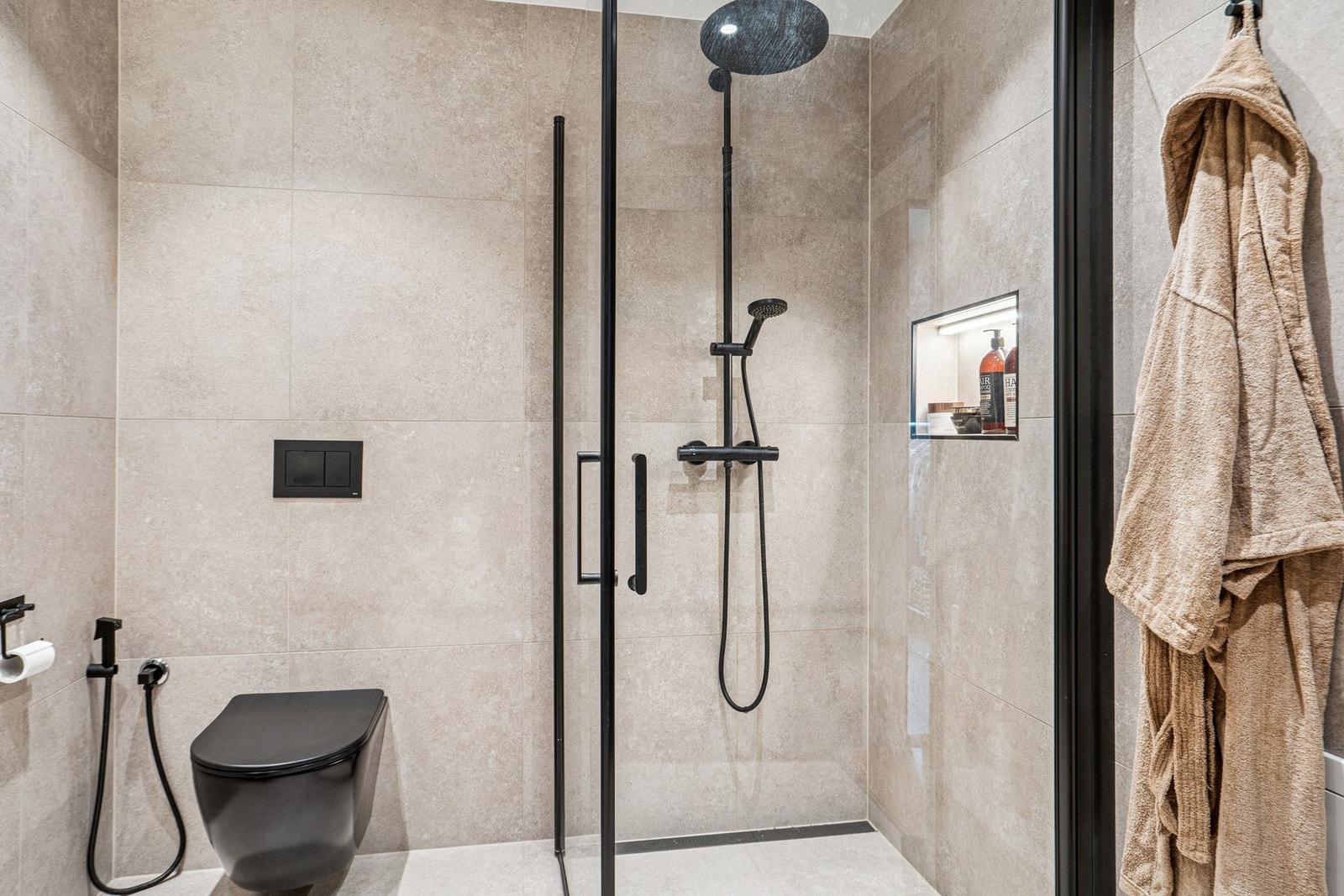 Dette baderommet er også utstyrt med vegghengt servantinnredning og vegghengt speil med lys, og et stilig dusjhjørne med innfellbare glassdører. Galleribilde