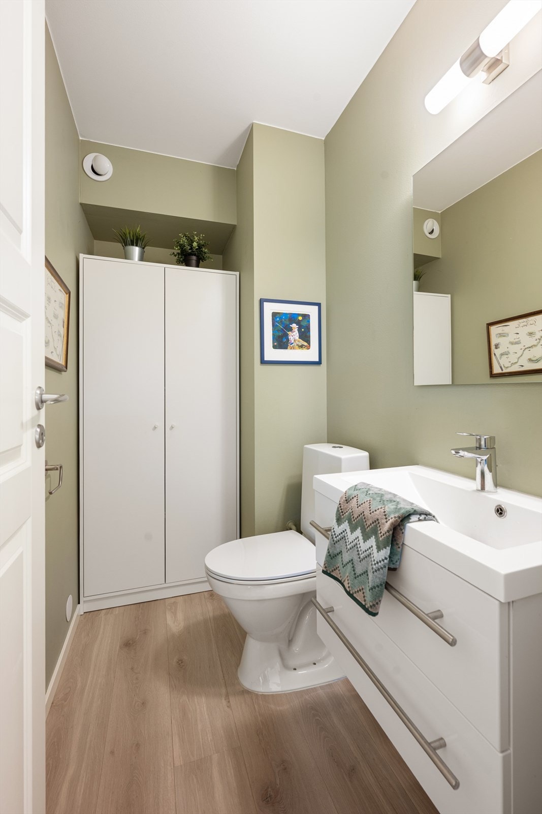 Praktisk toalettrom med gulvmontert toalett og enkel servant. God ventilasjonsløsning med felles avtrekk og luftespalte i døren sikrer et friskt og funksjonelt rom. Galleribilde