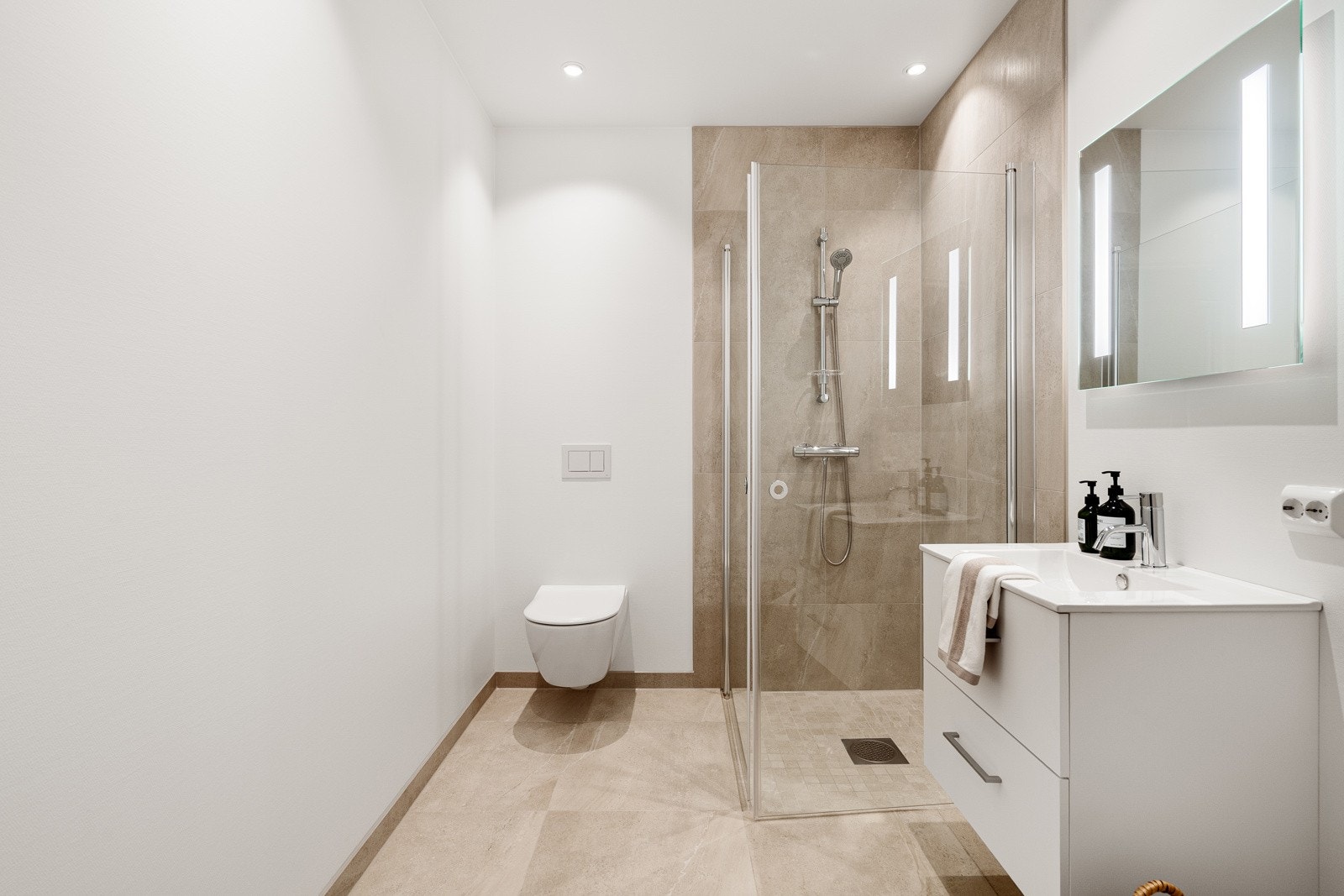 Nydelig bad med lekre fliser på gulv og i dusj-sone. Det er innredet med seksjon med nedfelt servant, toalett med innbygd sisterne og dusj med glassdører. Galleribilde