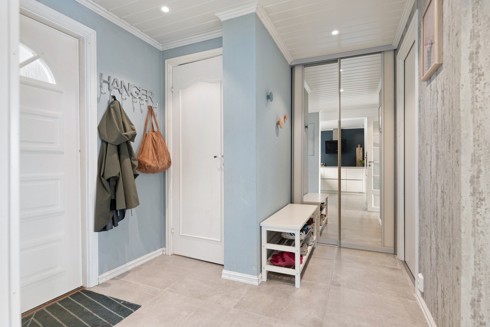 Vi ønskes velkommen av en lys entré med moderne gulvfliser, downlights i taket og skyvedørsgarderobe for ytterklær og sko. Galleribilde