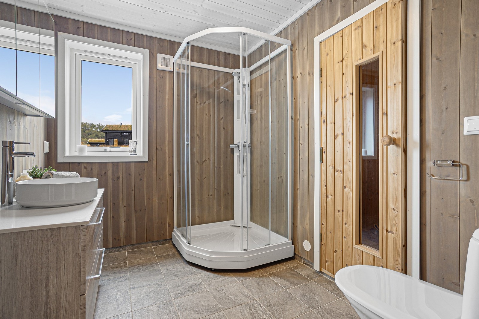 Lekkert hyttebad med flislagt gulv kombinert med lune, interiørbeisede vegger Galleribilde