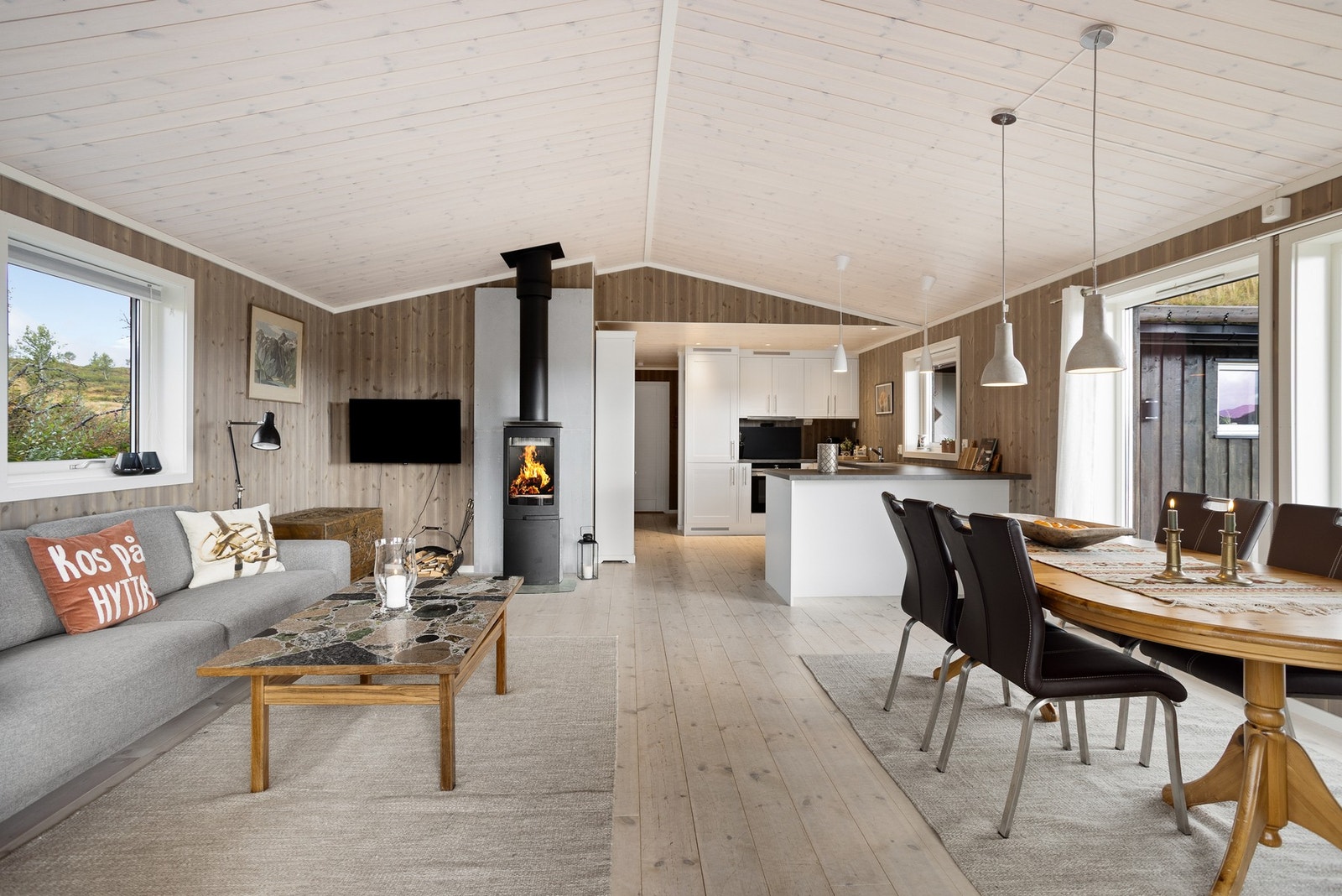 Nydelig, åpen stue/kjøkken-løsning med god takhøyde og store vinduer som bringer lyset og naturen inn i rommet Galleribilde