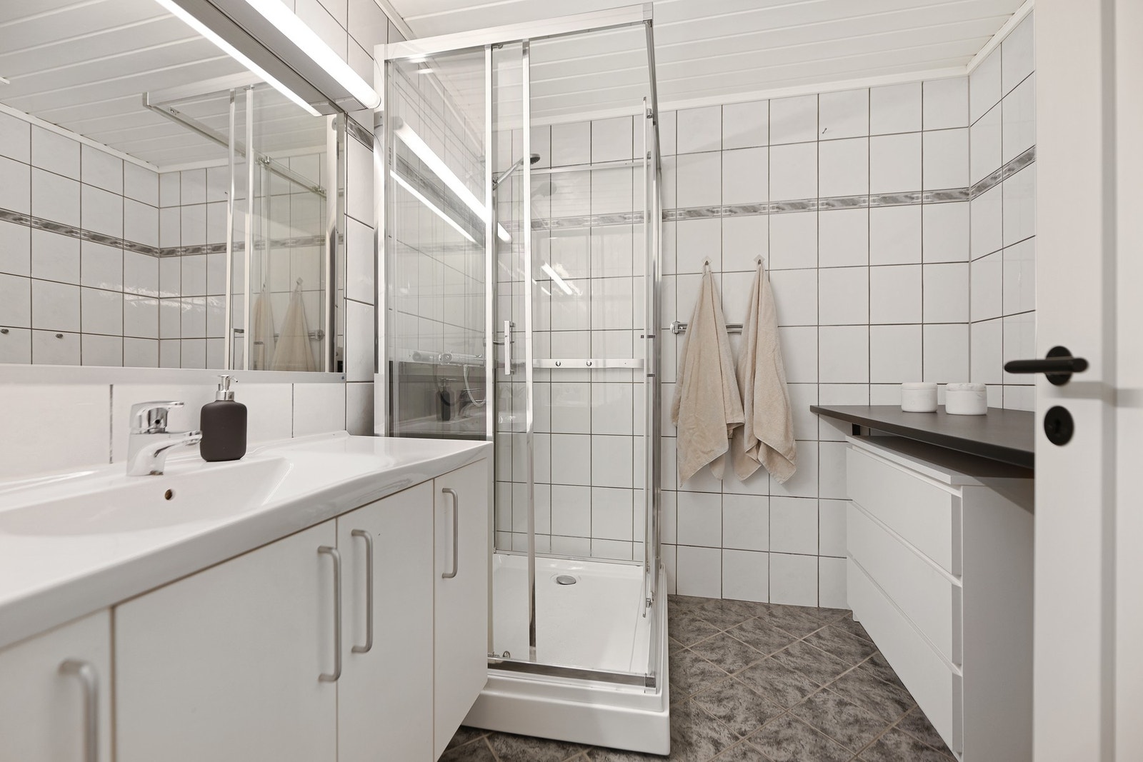 Badet i 2. etasje er flislagt, men med ukjent alder. Badet er praktisk plassert rundt boligens soverom. Rommet har innredning med nedfelt servant, dusjkabinett (fra 2020) og opplegg for vaskemaskin. Galleribilde